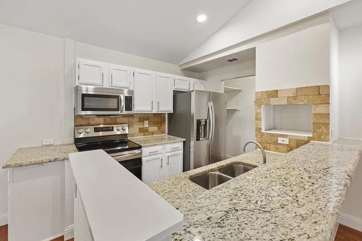 L-shaped kitchen with white cabinets, granite countertops, stainless fridge and range, subway tile backsplash, and an inviting, open layout