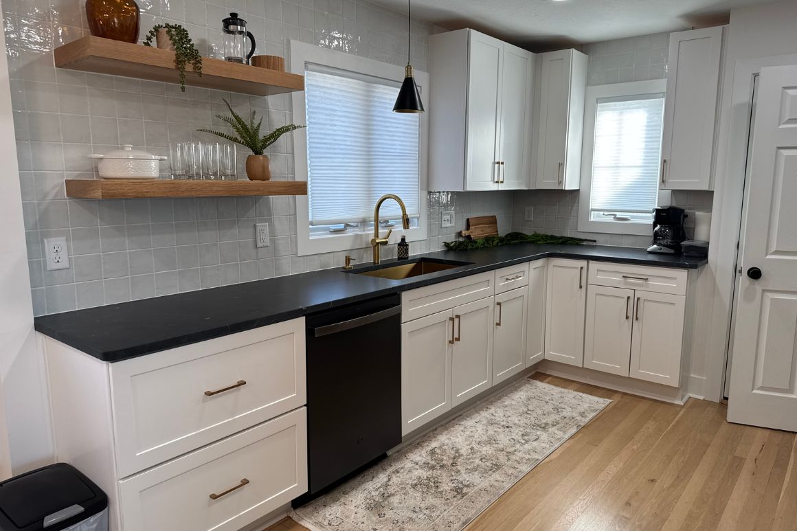 Open-concept kitchen featuring granite countertops, white cabinetry, black appliances, wood-look flooring, and a spacious, inviting layout