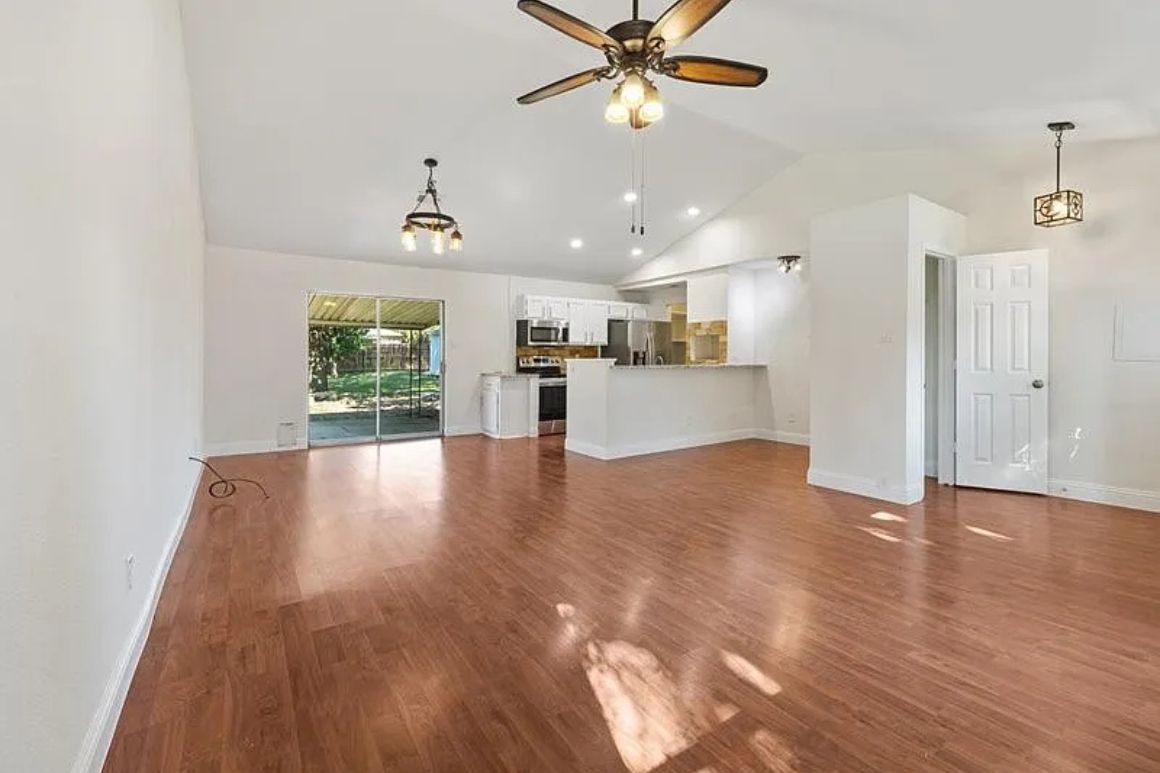 Open-concept kitchen with white cabinetry, granite countertops, light wood flooring, stainless appliances, and a generous living-dining flow