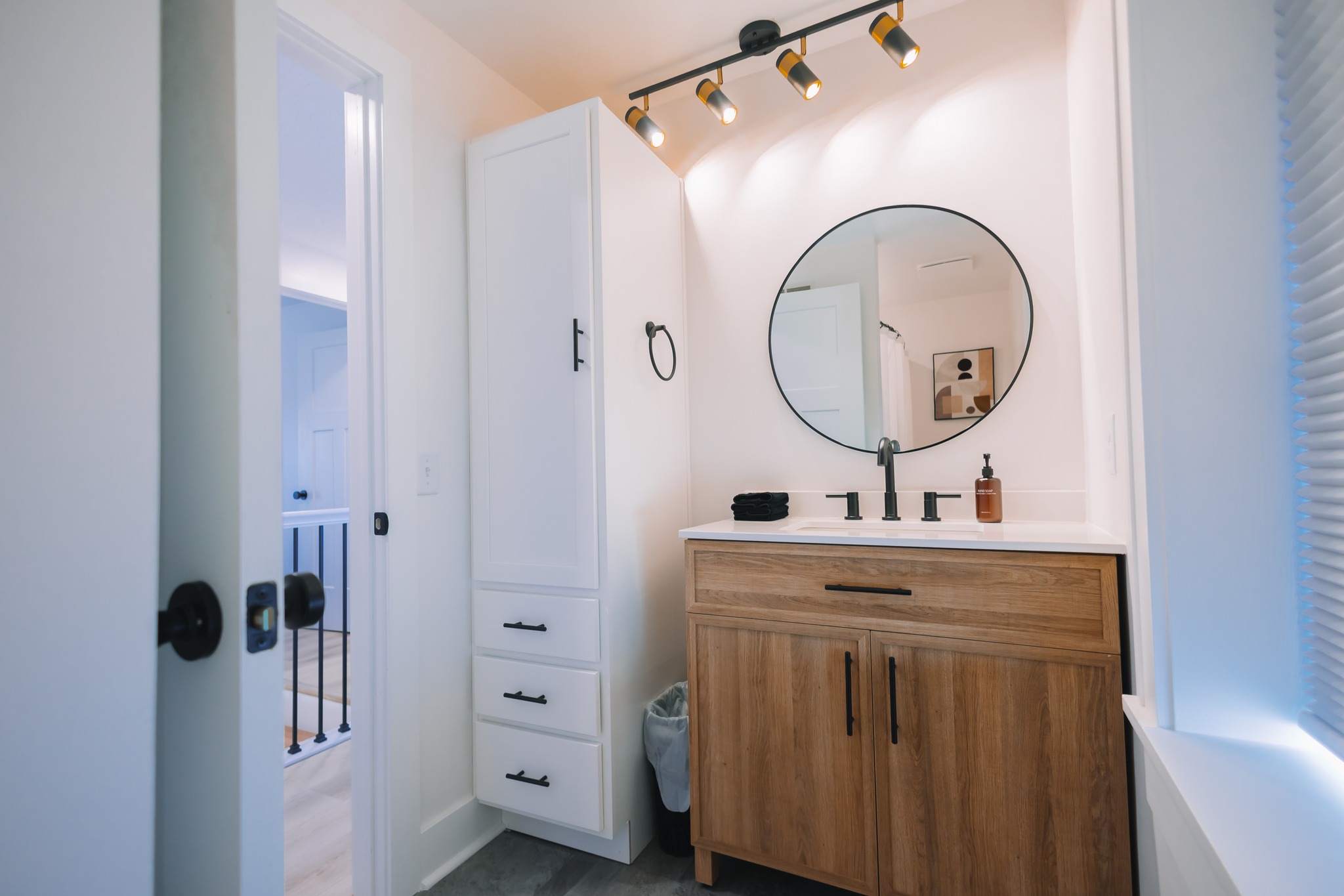 After Powder bathroom remodel in Flower Mound, TX featuring a wood vanity, round mirror, and modern black fixtures