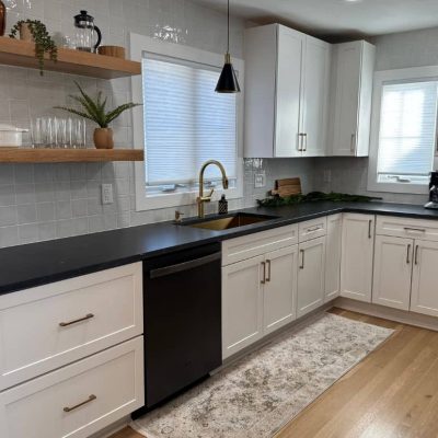 Open-concept kitchen featuring granite countertops, white cabinetry, black appliances, wood-look flooring, and a spacious, inviting layout